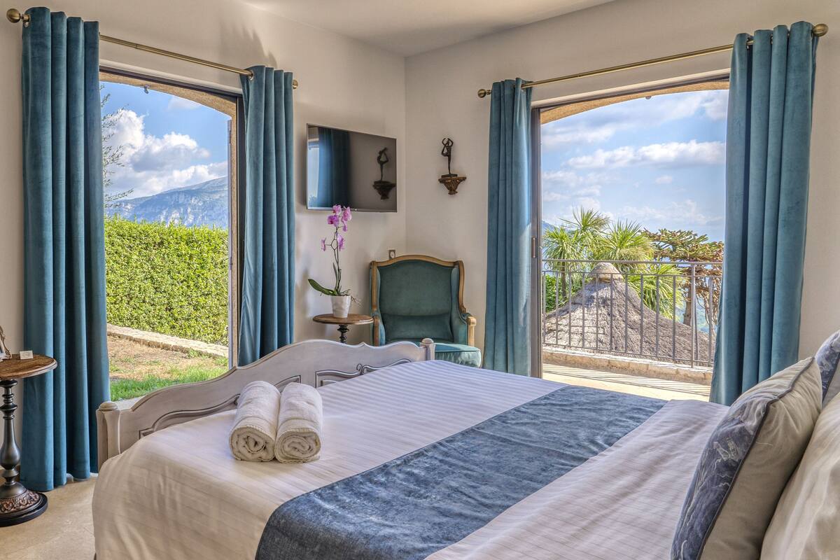 Habitación de hotel con una cama grande, una silla, una mesita y un televisor en la pared.