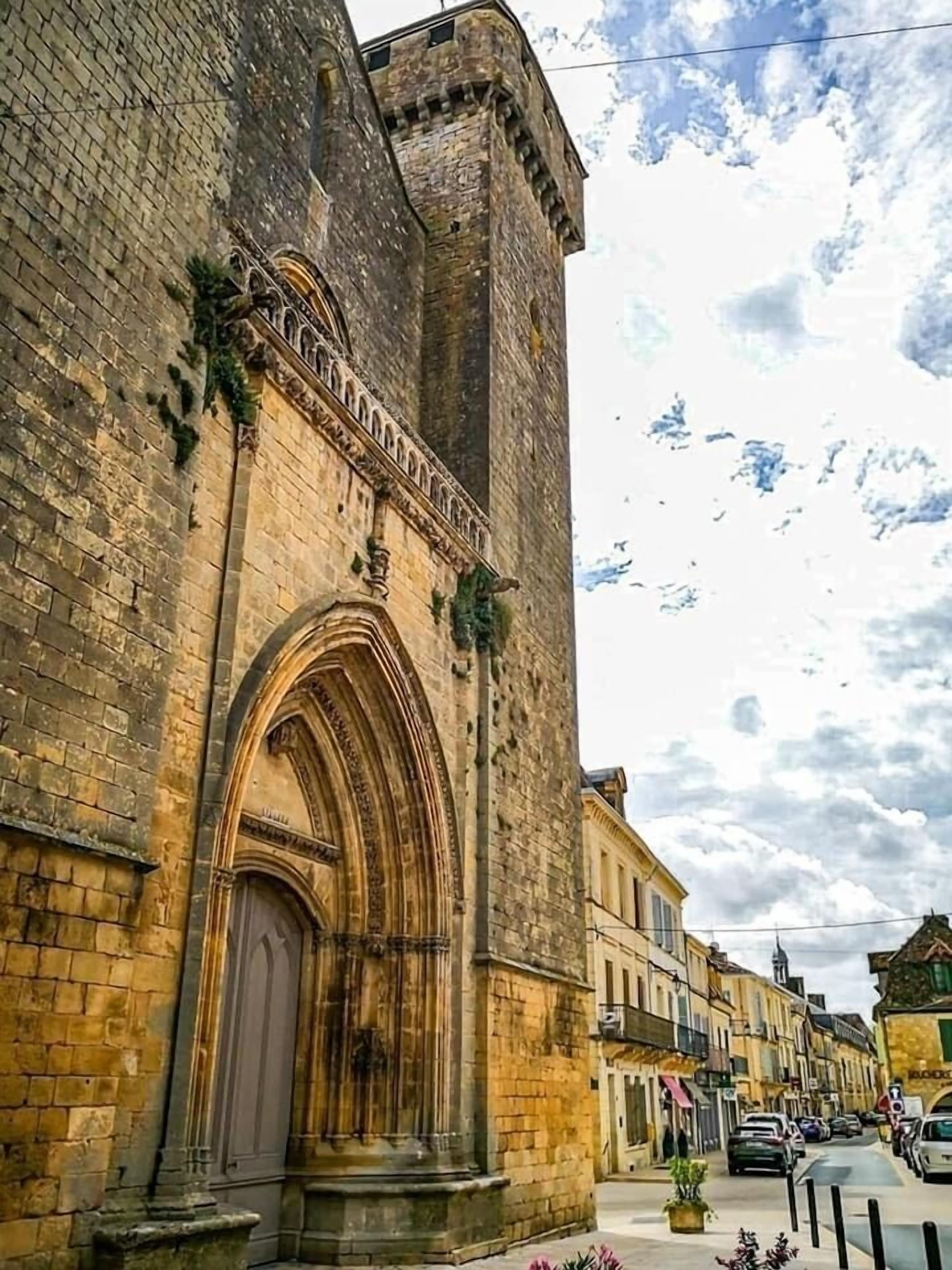 Um edifício histórico de pedra com uma grande entrada em arco e uma torre alta.