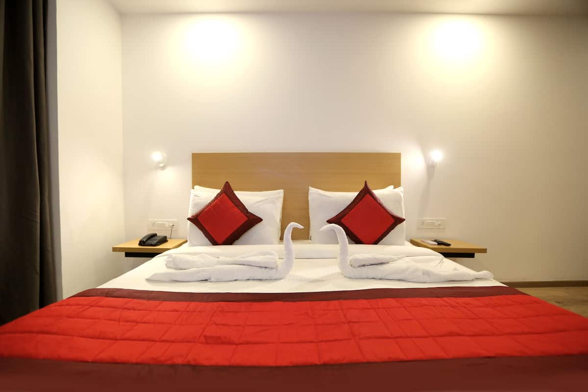 A hotel room with a neatly made bed, two nightstands, and a red bedspread.