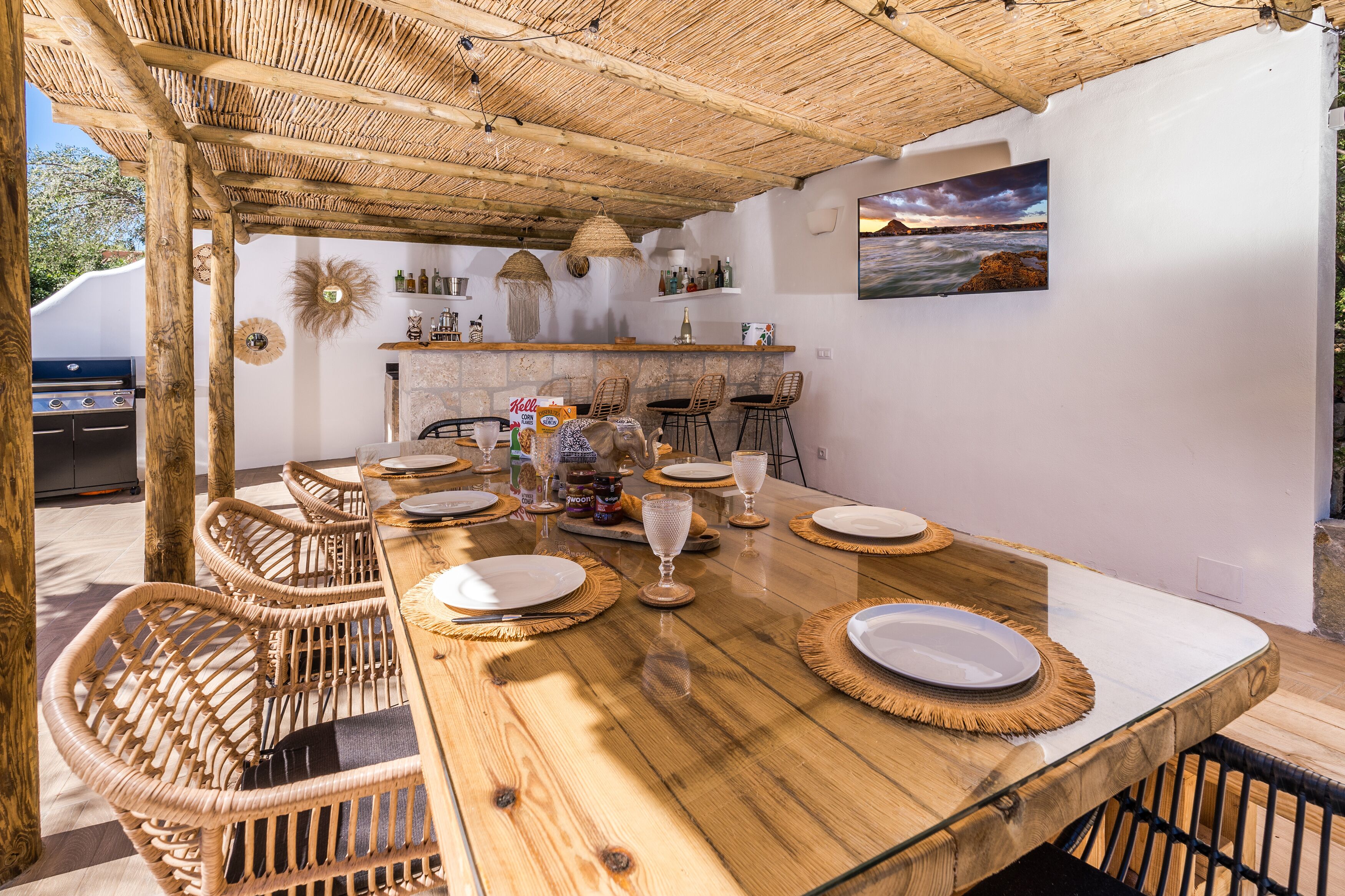 An outdoor dining area with a wooden table, wicker chairs, and a thatched roof.