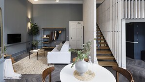 Un salon moderne avec un canapé blanc, une table à manger agrémentée d’un vase, un escalier et un téléviseur fixé au mur.