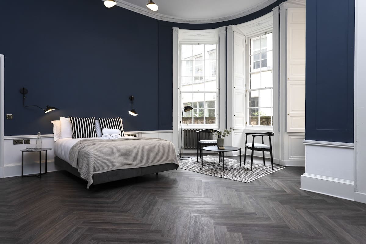 A bedroom with a bed, bedside lamps, a small table, and a chair.