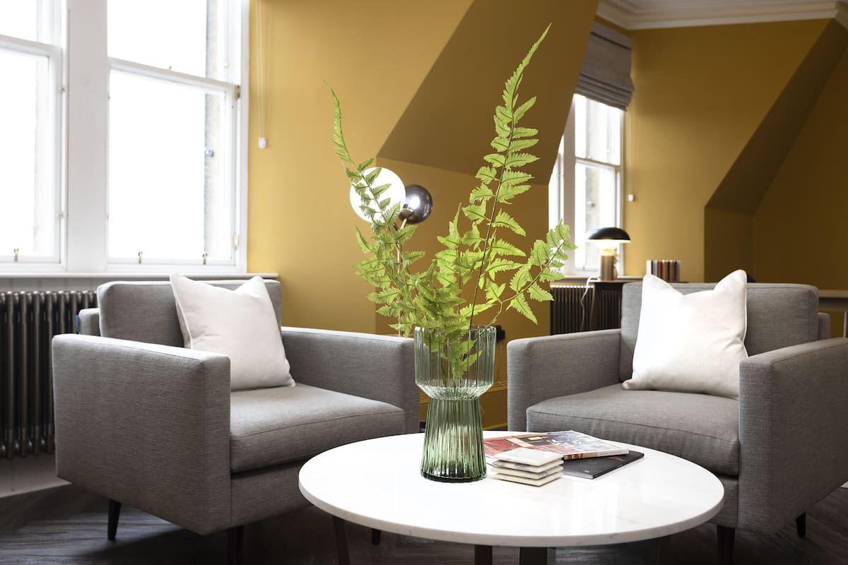 A modern living room with two grey sofas, a white coffee table, and a green plant in a glass vase.