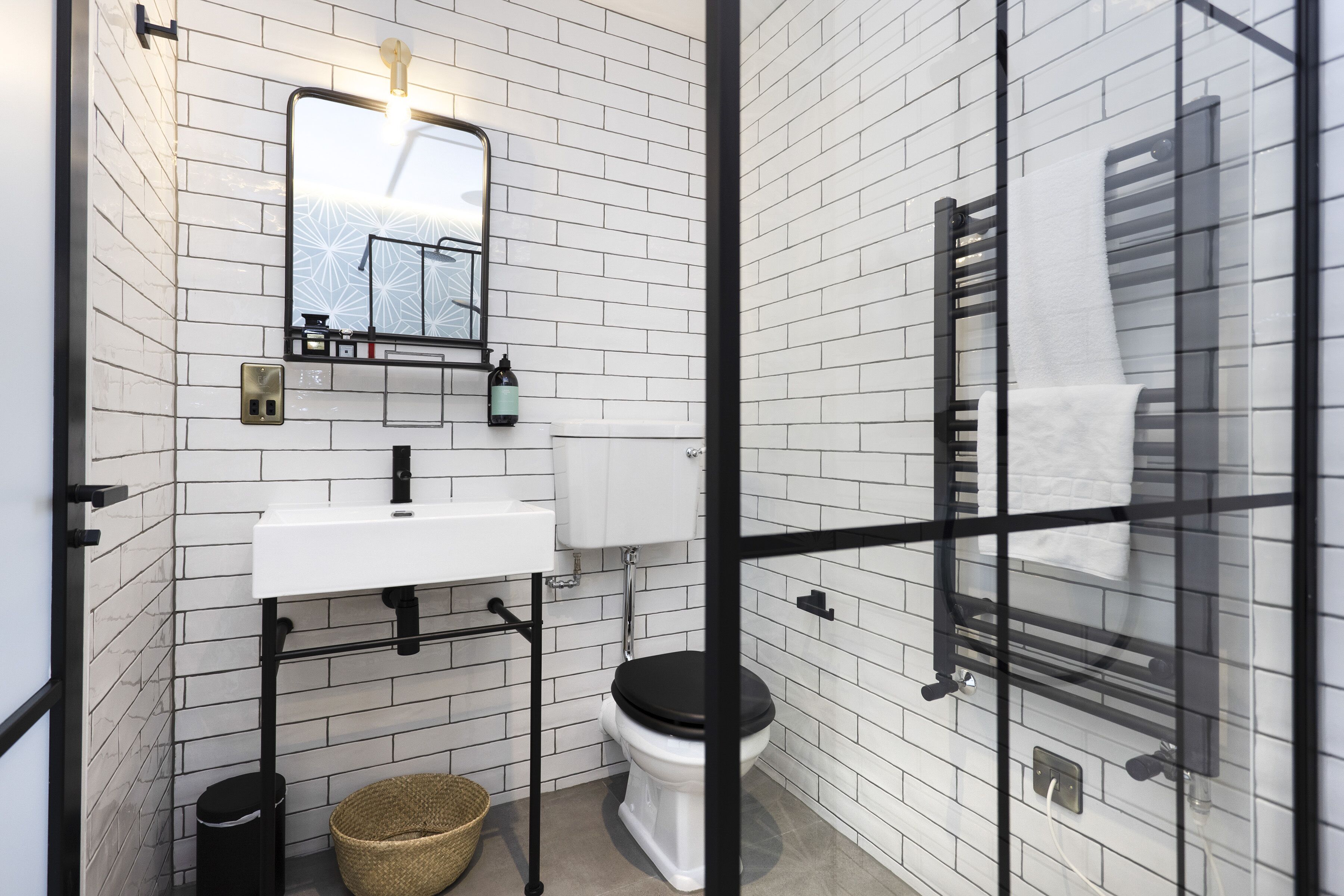 A modern bathroom with white subway tiles, a white sink, black toilet, and a glass shower enclosure.