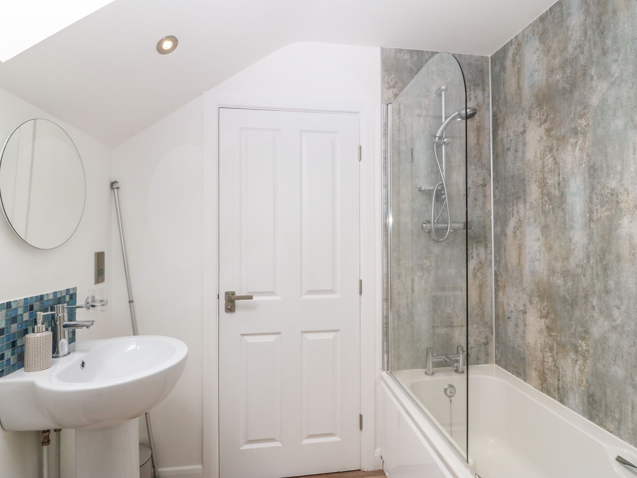 A bathroom with a white sink, a glass shower enclosure, and a white door.