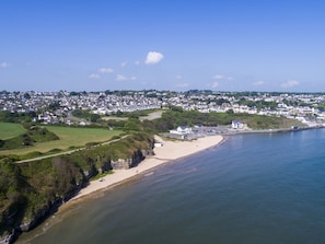 Vista aérea de uma cidade costeira com praia de areia, casas residenciais e céu azul límpido.