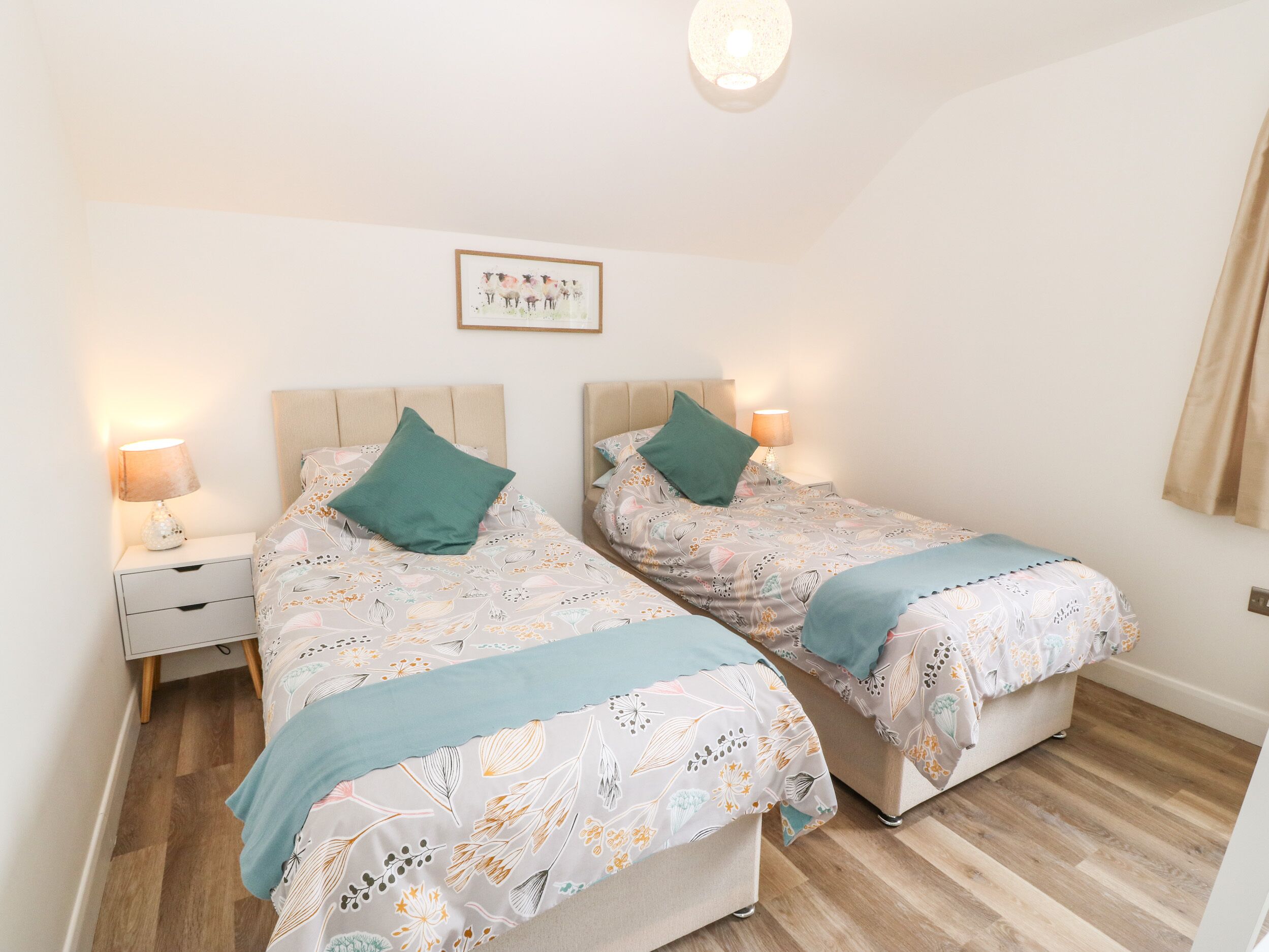 A bedroom with two beds, each with a headboard, a bedside table, and a lamp.