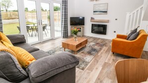 Una sala de estar moderna con un sofá gris, un sillón naranja, una mesa de centro de madera y un televisor.