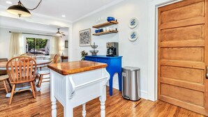 Uma área de refeições com uma mesa e cadeiras de madeira, um armário azul com eletrodomésticos de cozinha e uma lixeira.