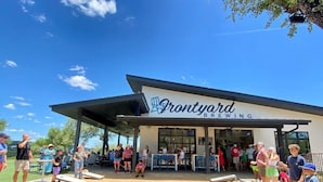 A building with a sign reading "Frontyard Brewing" and outdoor seating area with tables and chairs.