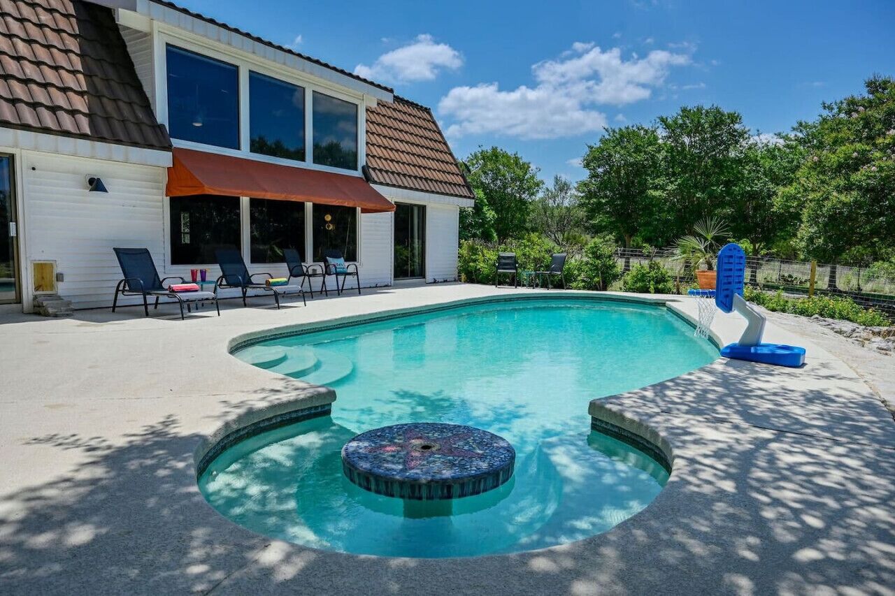 A house with a swimming pool, a hot tub, and a covered patio area with lounge chairs.