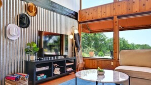 Ein gemütliches Wohnzimmer mit Fernseher, Holzmöbeln und Blick ins Grüne.