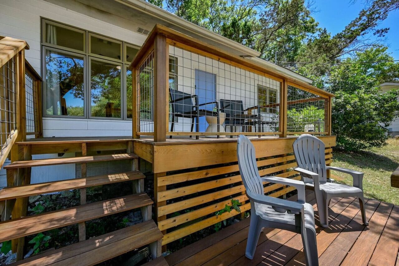 Una terraza de madera con un espacio de estar techado, una silla y una escalera que lleva a una casa.