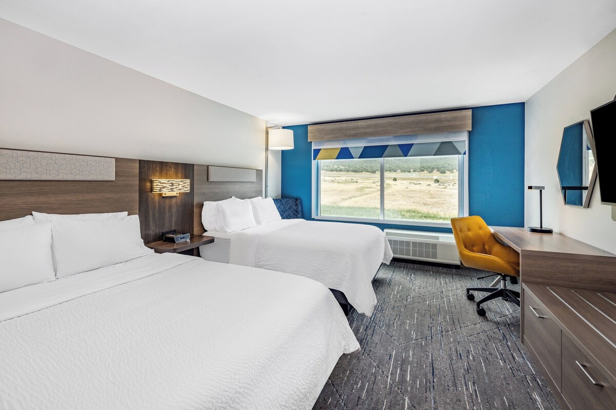 Quarto de hotel com duas camas, uma mesa, uma cadeira, televisão e janela com vista para o exterior.