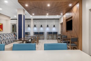 A modern dining area with wooden tables and chairs, a blue cushioned bench, and pendant lighting. - Holiday Inn Express & Suites Nephi by IHG (Nephi)