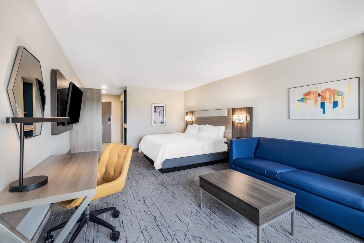 Une chambre d’hôtel moderne avec un lit, un canapé bleu, un bureau avec une chaise et un téléviseur.