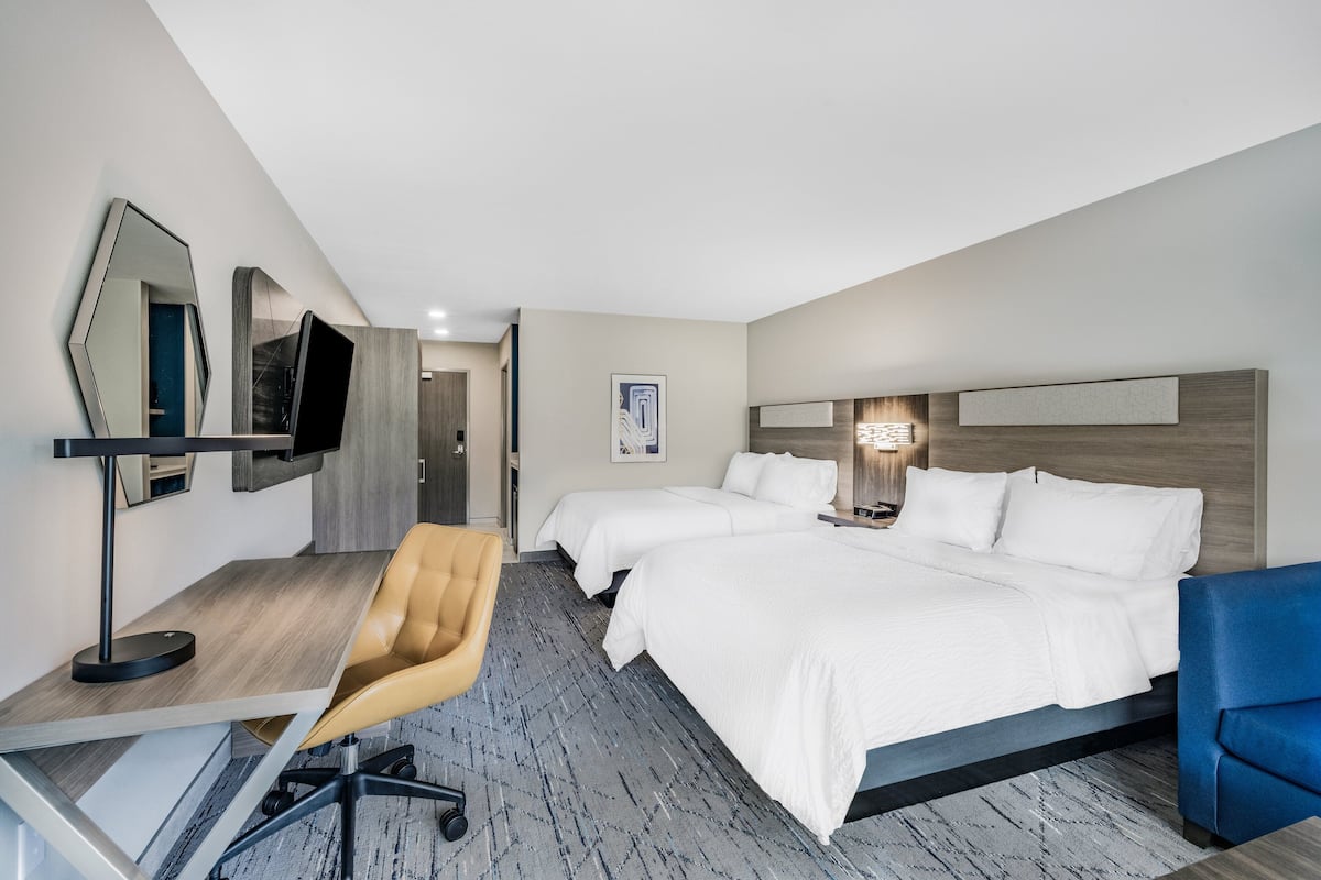 Une chambre d’hôtel avec deux lits, un bureau avec une chaise, une télévision, et une salle de bain visible au fond.