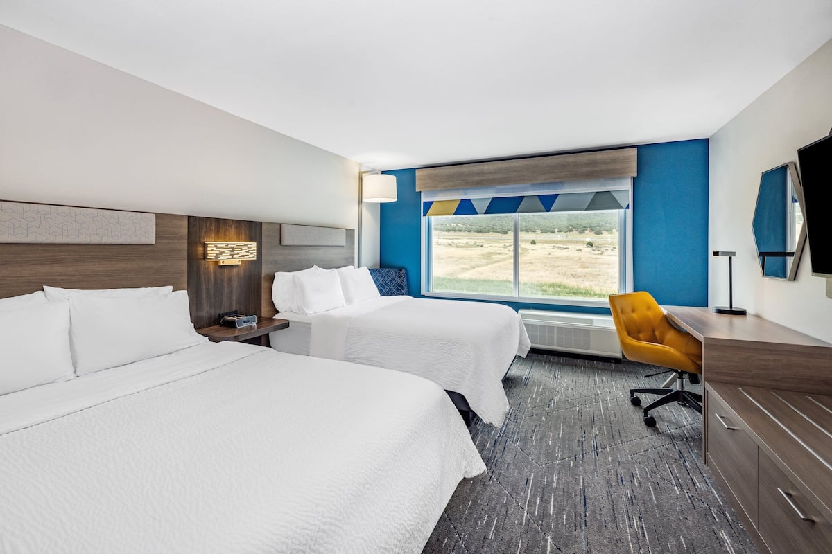 Une chambre d’hôtel avec deux lits, un bureau, une chaise, une télévision et une fenêtre donnant sur l’extérieur.