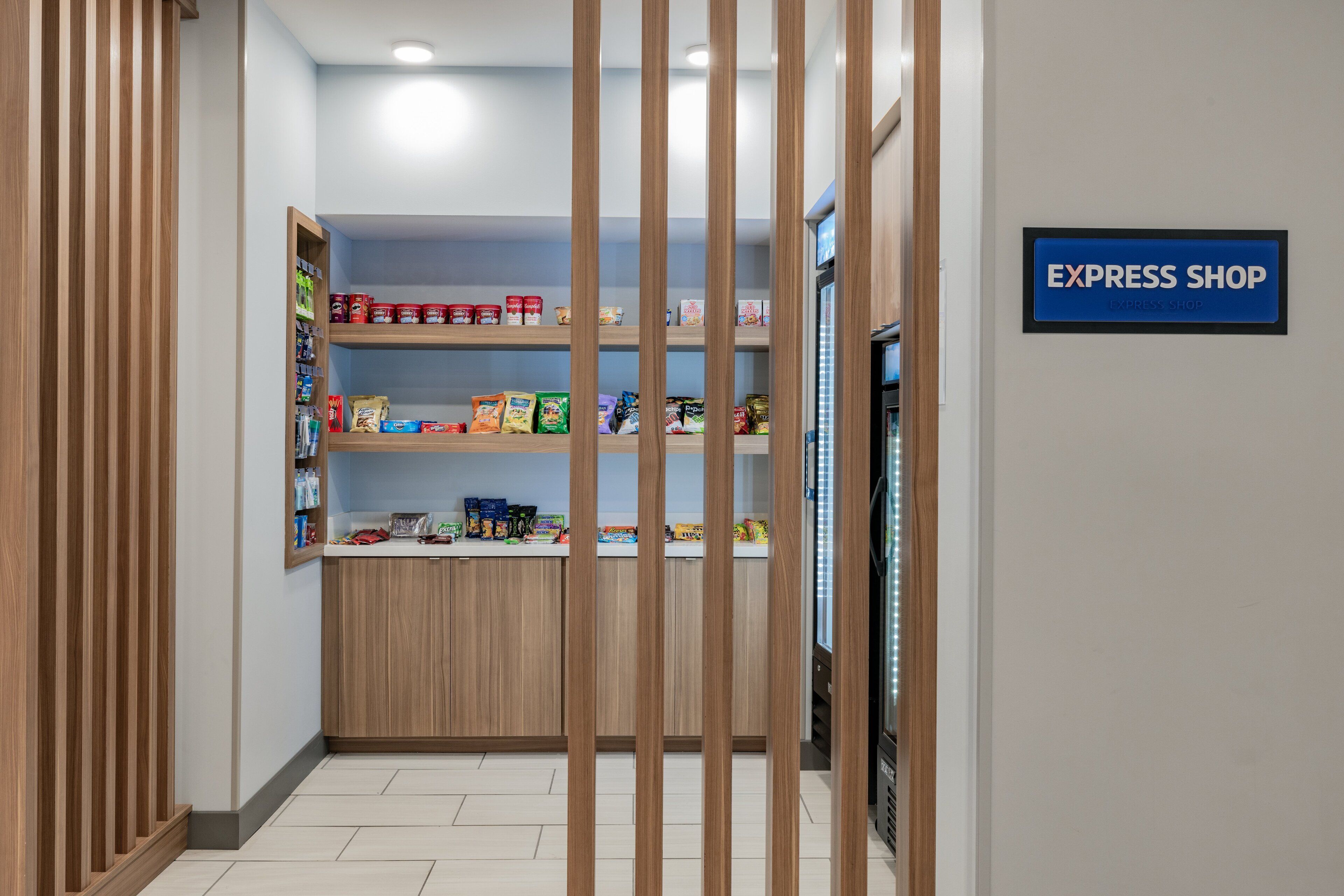 A corridor with a wooden partition, a refrigerated display case, and shelves stocked with various food items. A sign indicates the presence of an express shop.