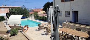 A pool area with lounge chairs and tables, surrounded by a building with a tiled roof. - Beautiful, air-conditioned studio with a swimming pool (Saint-Laurent-du-Var)