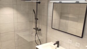 Un baño moderno con ducha envuelta en vidrio, un lavabo blanco sobre un mueble de madera y un espejo encima del lavabo.