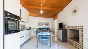 A modern kitchen with a built-in oven, a dining area with blue chairs, and a decorative fireplace. - Holiday Home 'Attico Lussu' with Sea View, Terraces & A/C (Villasimius)