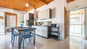 A modern kitchen with a wooden ceiling, white cabinets, a dining area with blue chairs, and a view through a glass door. - Holiday Home 'Attico Lussu' with Sea View, Terraces & A/C (Villasimius)