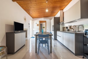 A modern kitchen with a wooden ceiling, a dining table with chairs, and a TV on a cabinet.
