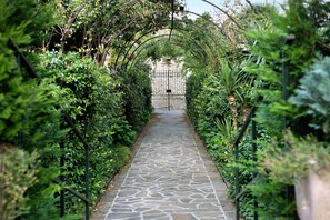 Ein gepflasterter Weg führt durch einen Garten mit einer bogenförmigen Metallkonstruktion.