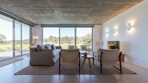 Ein geräumiges Wohnzimmer mit großem Fenster, einer Couch, Sesseln, einem kleinen Tisch und einem Kamin.