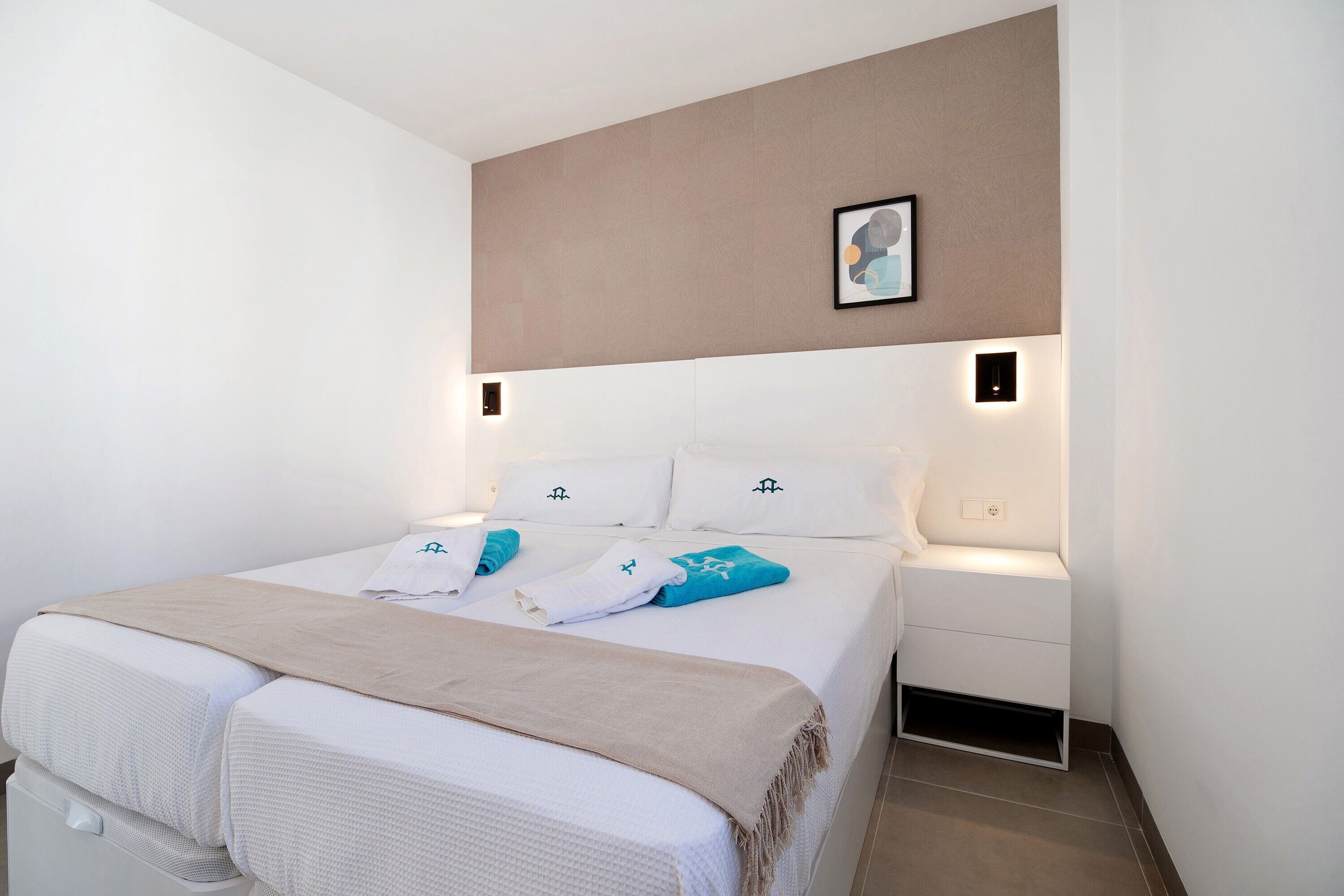 Un dormitorio ordenado con cama, mesitas de noche y una lámpara fijada a la pared.