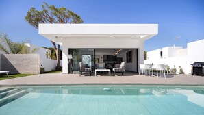 Une maison moderne avec une piscine, un espace salon extérieur et un ciel dégagé.