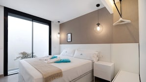 Une chambre moderne avec un grand lit, des tables de chevet, un luminaire suspendu et une vue sur l’extérieur grâce à une porte coulissante.