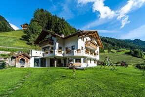 A two-story chalet with a balcony, a stone oven, and a view of a green valley.