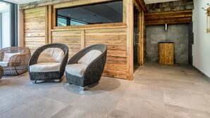 Ein Zimmer mit einer Holzwand, zwei Korbstühlen mit Kissen, einem Steinkamin und einem großen Fenster.