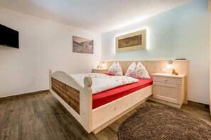 A bedroom with a wooden bed, a red mattress, two bedside tables, a wall-mounted TV, and a framed picture. - Apartment "Kreuzkofel" with Shared Whirlpool & Garden (Valle Aurina)