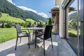 A patio with a table and chairs, a stone floor, and a view of a green valley and mountains. - Apartment "Kreuzkofel" with Shared Whirlpool & Garden (Valle Aurina)