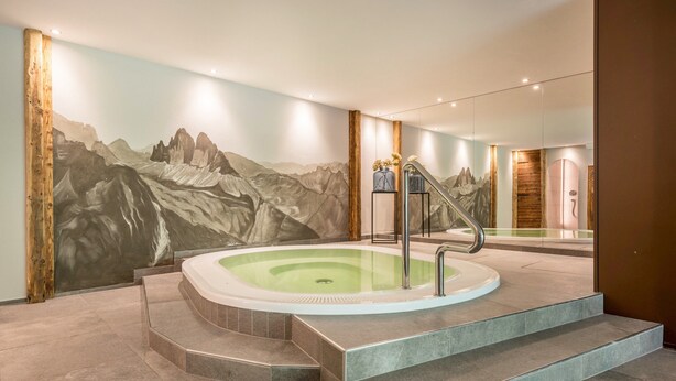 Ein Wellnessbereich mit Whirlpool, Treppe davor und Wandgemälde mit Bergmotiv.