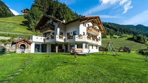 Eine zweistöckige Chalet mit Balkon, Steinofen und Blick auf ein grünes Tal.