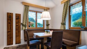 A dining area with a wooden table, four chairs, a bench, and a hanging light fixture. - Apartment "Schwarzenstein" with Shared Whirlpool & Garden (Valle Aurina)
