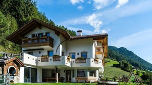A two-story chalet with balconies, a stone entrance, and a grassy yard. - Apartment "Schwarzenstein" with Shared Whirlpool & Garden (Valle Aurina)