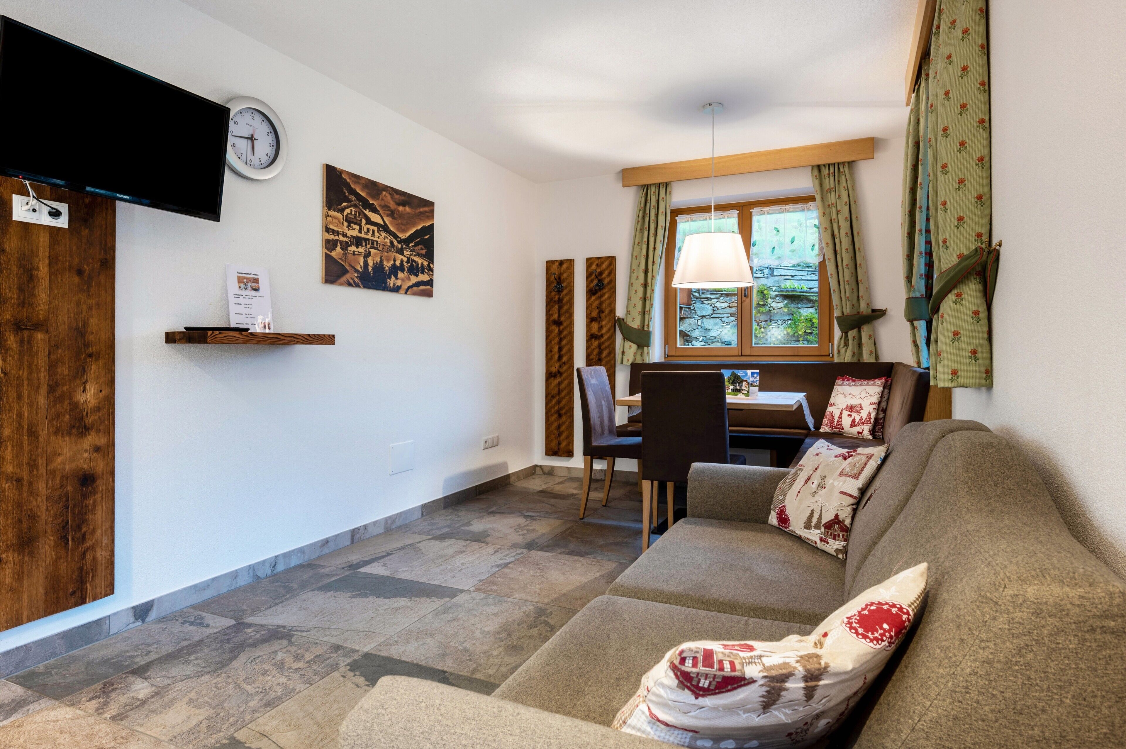 Un salon comprenant un canapé, un téléviseur fixé au mur, une étagère en bois, une table à manger avec des chaises et une fenêtre avec des rideaux.
