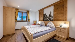 A bedroom with a wooden bed, a nightstand, a window with curtains, a painting on the wall, and a wooden wardrobe.