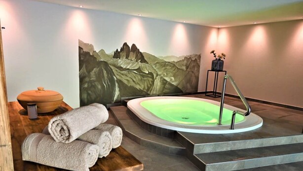 A spa room with a hot tub, towels, a painting, and a small table with a pot.