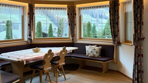 A room with a wooden ceiling, large windows with curtains, a table with chairs, and a bench with cushions. - Holiday Apartment "Weiße Zinne" with Shared Whirlpool & Garden (Valle Aurina)