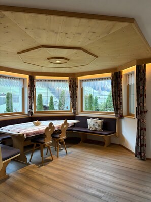 Una habitación con techo de madera, ventanas amplias con cortinas, una mesa con sillas y un banco con cojines.