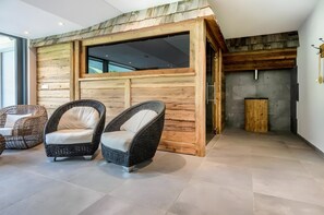Una habitación con pared de madera, dos sillas de mimbre, una chimenea y un ventanal grande.