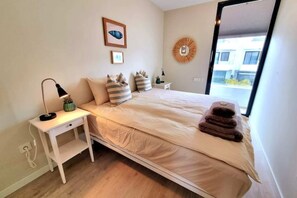 A bedroom with a bed, bedside table, lamp, and a window with a view.