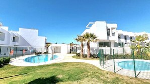 A modern residential area with white buildings, a swimming pool, and palm trees. - Holiday Home 'Modern Terrassed House Close Beach' with Sea View and Wi-Fi (Málaga)