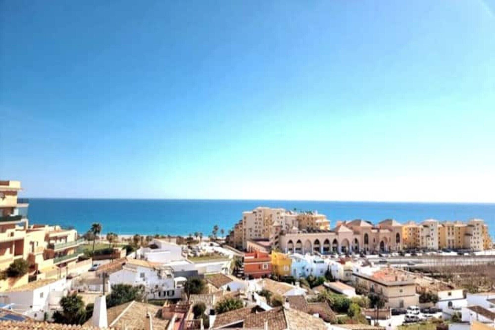 A coastal town with buildings, a clear sky, and the sea in the background.